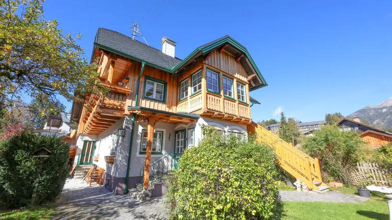 Traditionelles Holzhaus mit Balkonen und gepflegtem Vorgarten unter blauem Himmel.