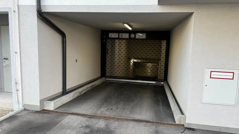 Einfahrt zur Tiefgarage eines modernen Wohngebäudes mit Rolltor und Entwässerungsrinne.