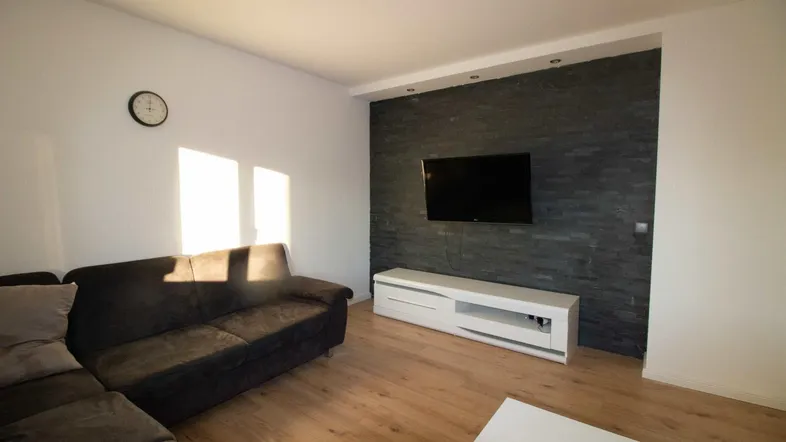 Helles Wohnzimmer mit modernem Design, Holzboden und einer Akzentwand mit Fernseher.