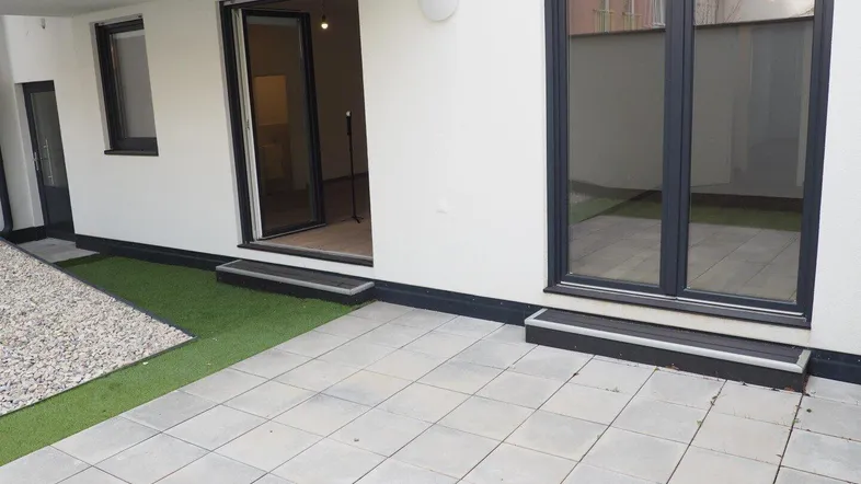 Geräumige Terrasse mit Steinplatten und Kunstrasen, ideal für entspannte Stunden im Freien.