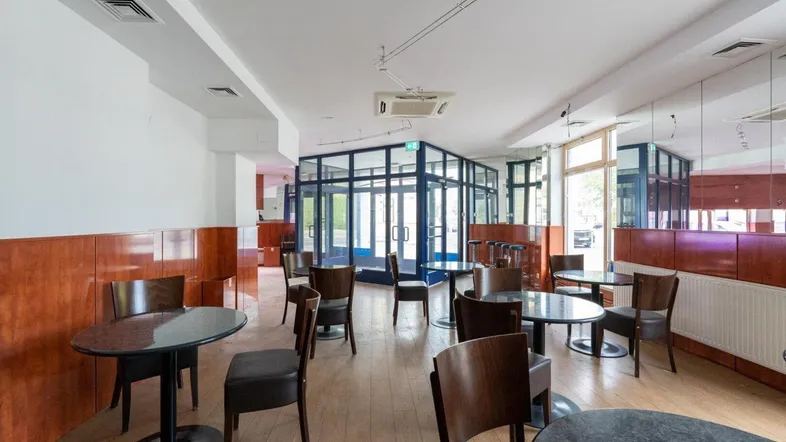 Geräumiger Gewerberaum mit Tischen, Stühlen und großen Fenstern, ideal für ein Café oder eine Bar.