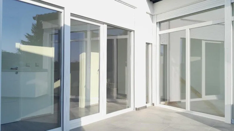 Helle, geflieste Terrasse mit großen Glasschiebetüren, die viel Tageslicht in die Innenräume lassen.