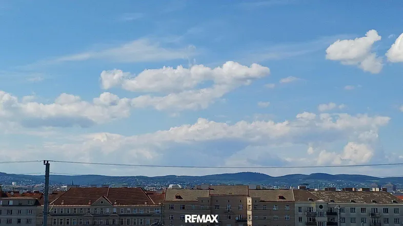 Panoramablick über die Stadt mit Bergen im Hintergrund unter einem weiten blauen Himmel.
