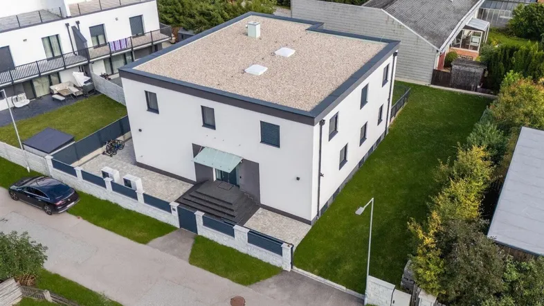 Modernes Einfamilienhaus mit Flachdach, weißer Fassade und gepflegtem Rasen in einer Wohnsiedlung.