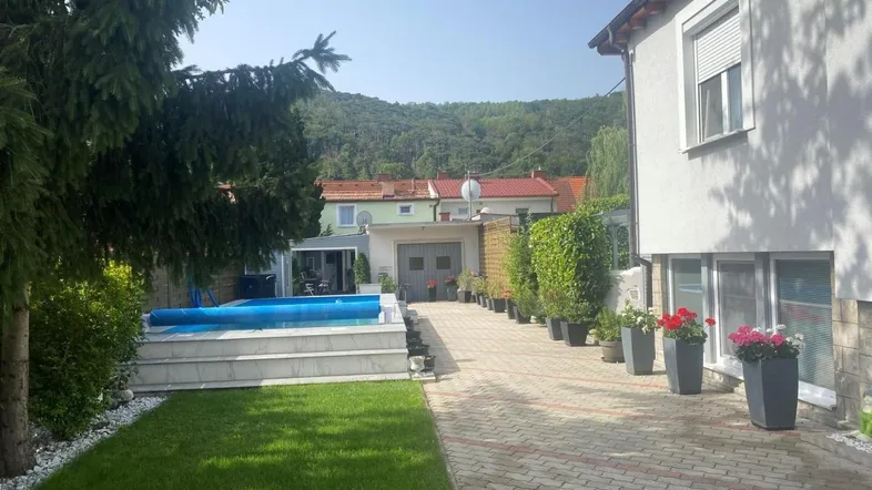 Außenbereich des Hauses mit Swimmingpool, gepflegtem Rasen und gepflasterter Auffahrt vor hügeliger Landschaft.