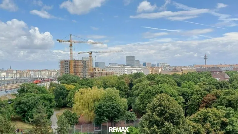 Weitläufiger Blick über die Stadt mit viel Grün, Baustellen und Zugverkehr.