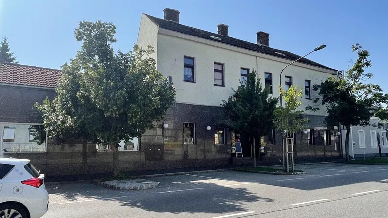 Ansicht des Gebäudes von der Straße mit Parkplätzen und Bäumen an einem sonnigen Tag.