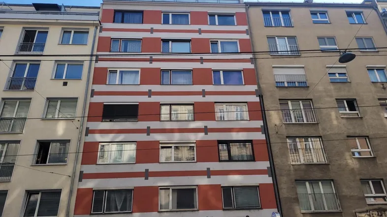Mehrstöckiges Wohngebäude mit rot-weiß gestreifter Fassade in einer städtischen Umgebung.