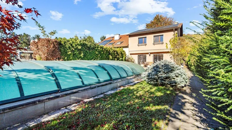Gartenbereich mit überdachtem Pool und einem Haus im Hintergrund unter blauem Himmel.