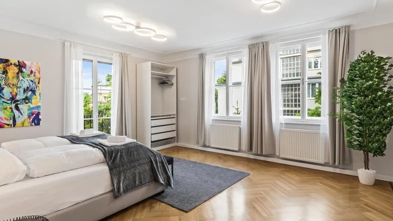 Helles Schlafzimmer mit Fischgrätparkett, großen Fenstern und offenem Kleiderschrank.