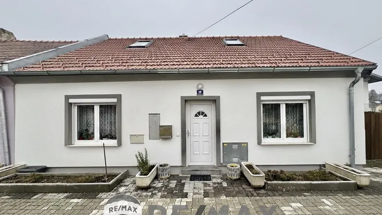 Einfamilienhaus mit weißer Fassade, roten Dachziegeln und kleinen Vorgartenbeeten.