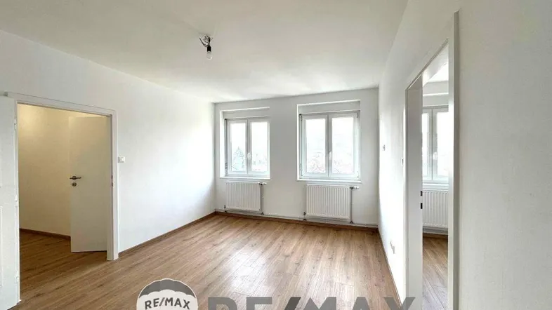 Helles, leeres Zimmer mit Holzfußboden und zwei Fenstern, bereit zur individuellen Gestaltung.