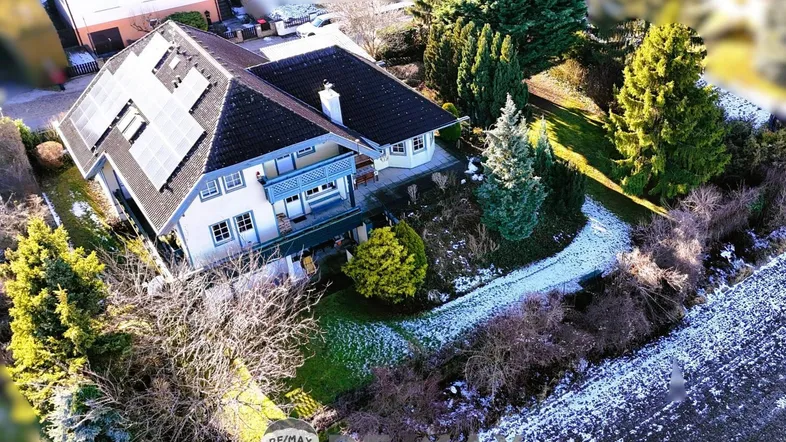 Luftaufnahme eines Einfamilienhauses mit Solaranlage auf dem Dach und umliegendem Garten im Winter.