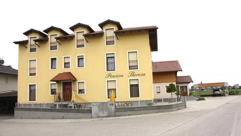 Gelbes Pensionsgebäude mit mehreren Stockwerken und Dachgauben, umgeben von einer kleinen Straße und Grünflächen.