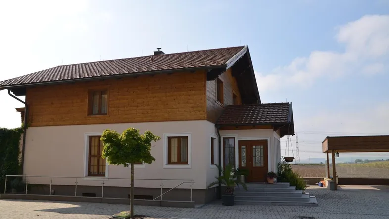 Traditionelles Einfamilienhaus mit Holzverkleidung und gepflastertem Vorplatz unter blauem Himmel.