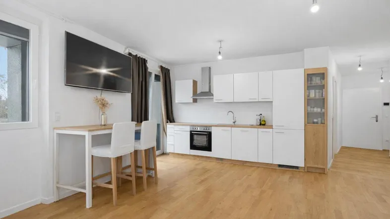 Moderne offene Wohnküche mit weißen Schränken, Holzboden und Bartresen für geselliges Beisammensein.