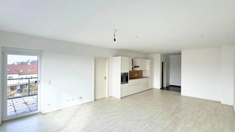 Heller, offener Wohnbereich mit integrierter Küche und Zugang zu einem kleinen Balkon.