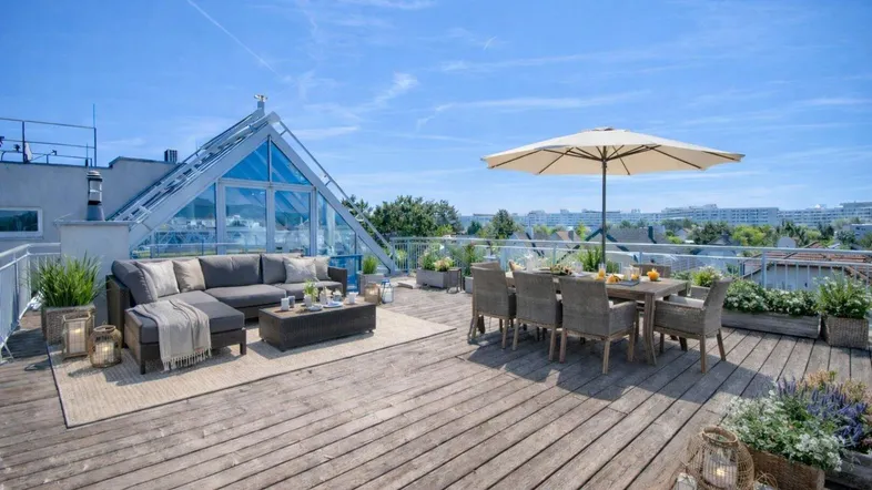 Große Dachterrasse mit gemütlicher Lounge und Essbereich, umgeben von Pflanzen und mit Stadtblick.