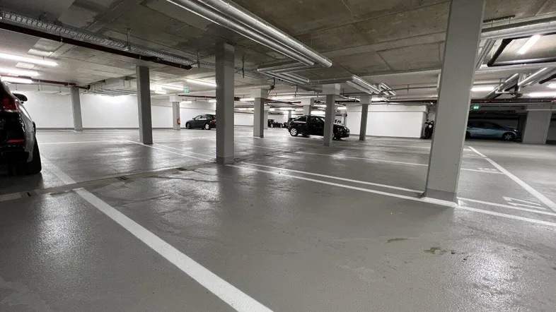 Geräumige Tiefgarage mit mehreren Stellplätzen, Betonpfeilern und sichtbaren Installationen.