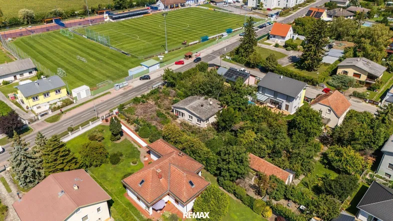 Luftaufnahme eines Wohngebiets mit Häusern, viel Grün und einem Sportplatz in der Nähe.