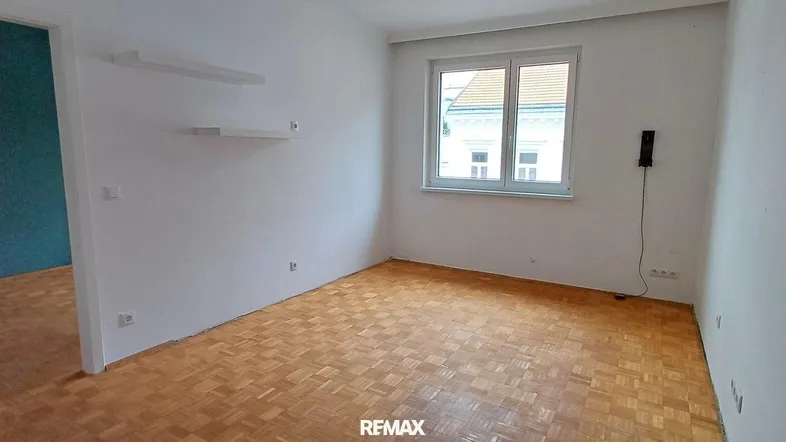 Helles Zimmer mit Parkettboden und einer Akzentwand, ideal als Wohn- oder Schlafzimmer nutzbar.