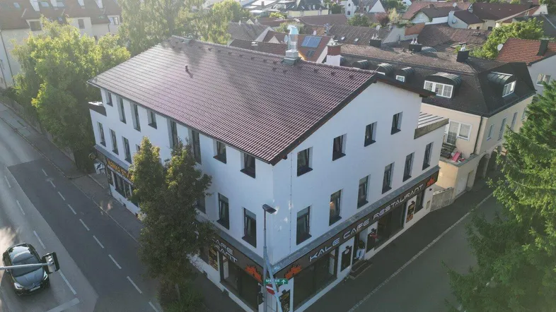 Luftaufnahme eines Gebäudes an einer Straßenecke mit umliegenden Wohnhäusern und viel Grün.