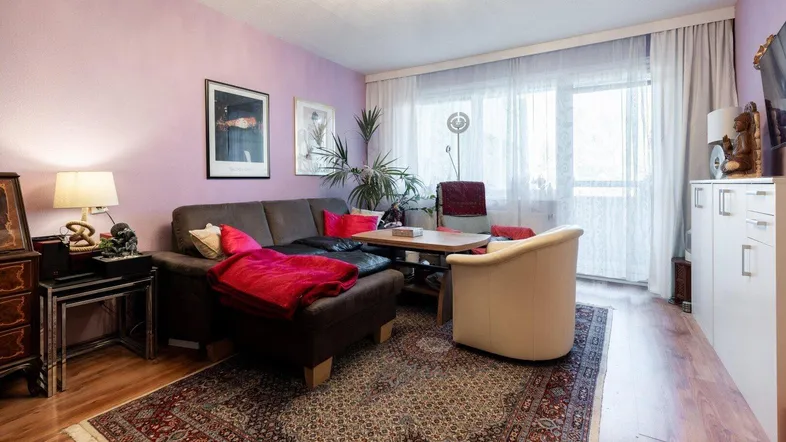 Gemütliches Wohnzimmer mit lila Wänden, Holzboden und Zugang zum Balkon.