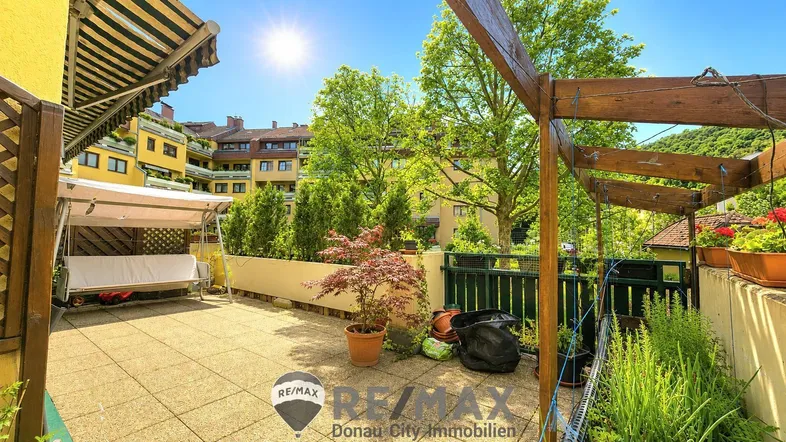 Sonnige Terrasse mit Markise, Schaukel und Blick auf die umliegenden Gebäude und Bäume.