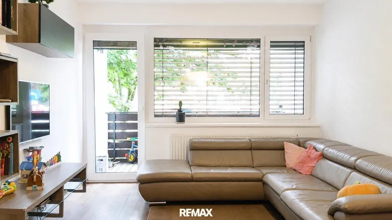 Helles Wohnzimmer mit beiger Ledercouch, Holzboden und Zugang zur Loggia.