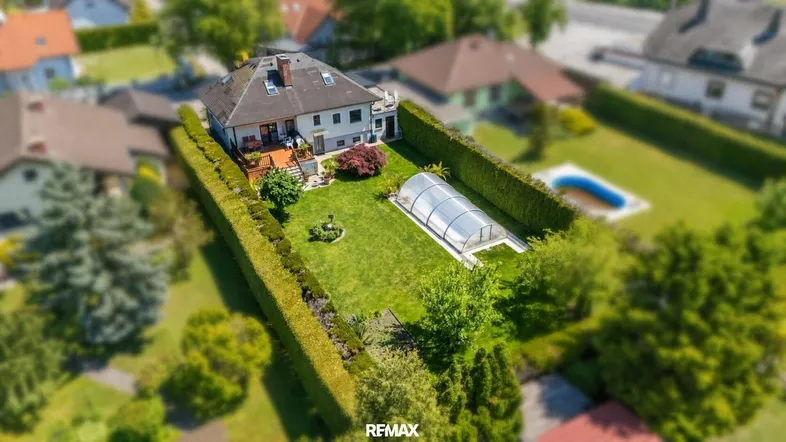 Luftaufnahme eines Einfamilienhauses mit großem Garten, überdachtem Pool und weiterer Poolanlage.