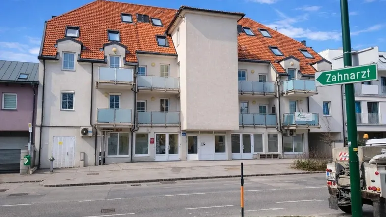 Mehrfamilienhaus mit mehreren Balkonen und Geschäften im Erdgeschoss an einer Straße.