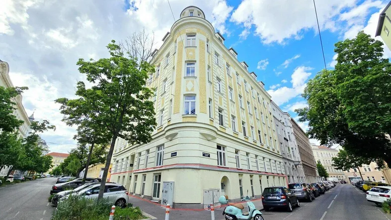 Historisches Eckgebäude mit gelber Fassade und vielen Fenstern an einer belebten Straße.