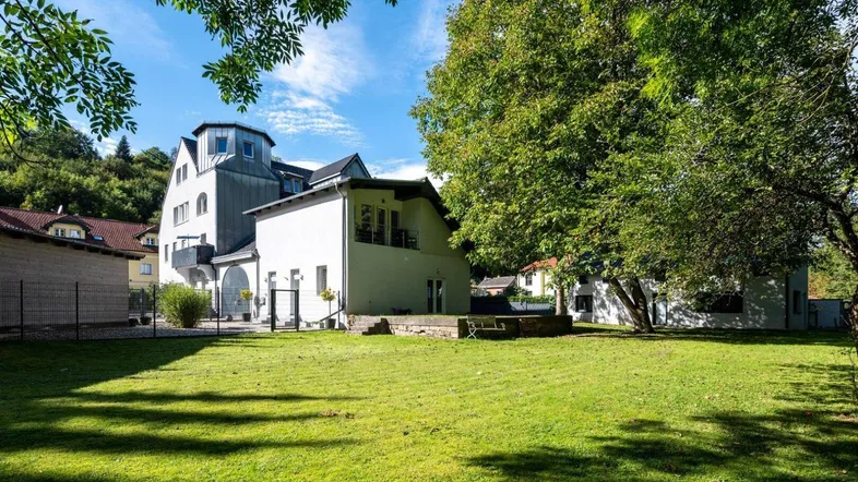 Großzügiger Gartenbereich mit altem Baumbestand und Blick auf das Wohngebäude unter blauem Himmel.