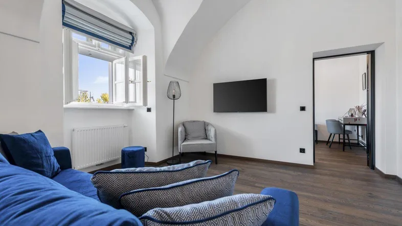 Helles Wohnzimmer mit blauer Couch, Holzboden und Blick nach draußen durch ein Bogenfenster.