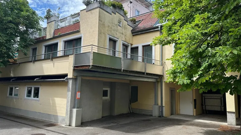 Gelbes Mehrfamilienhaus mit Balkonen, Terrassen und überdachtem Parkplatzbereich.