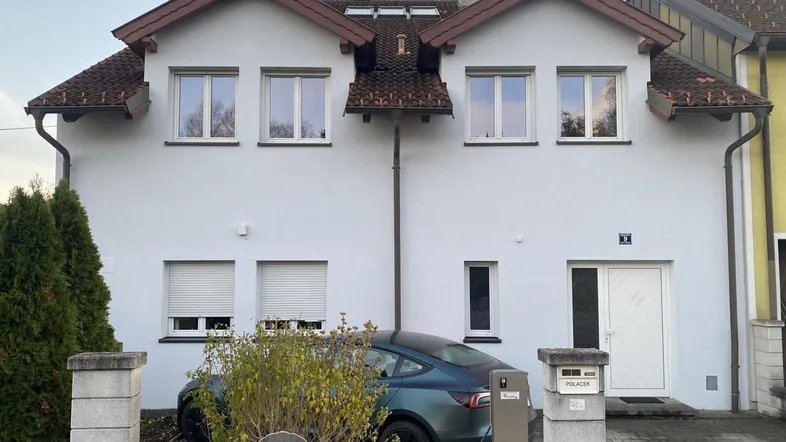 Weiße Hausfassade mit Satteldach, mehreren Fenstern und einem geparkten Auto davor.