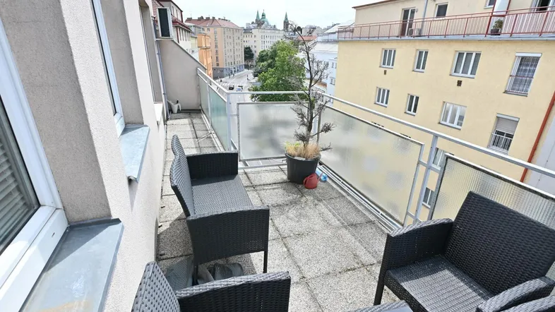Geräumiger Balkon mit Sitzgelegenheiten und Blick auf die Stadt und umliegende Gebäude.