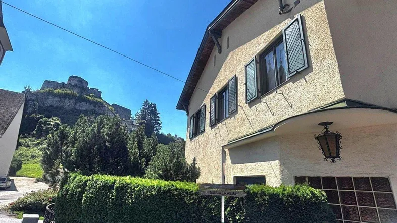Traditionelles Haus mit grünen Fensterläden und Blick auf eine historische Burgruine.