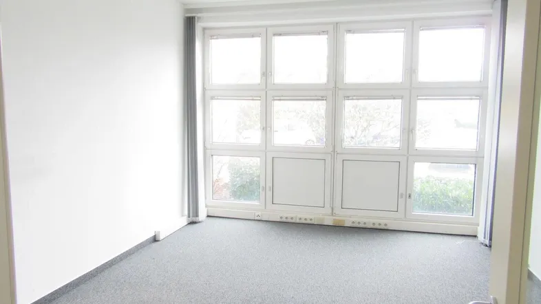 Heller Büroraum mit Teppichboden und großen Fenstern, ideal für Arbeitsplätze.