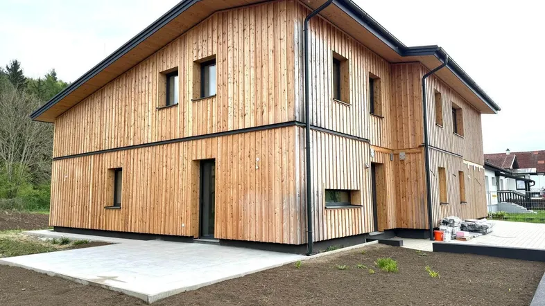 Neubau-Doppelhaushälfte mit Holzfassade und noch unfertigem Außenbereich.