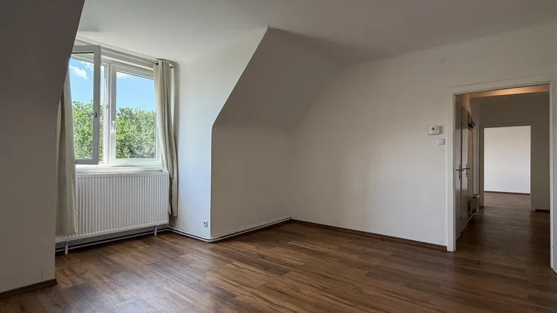 Helles Zimmer mit Dachschrägen, Laminatboden und Blick ins Grüne durch das Fenster.