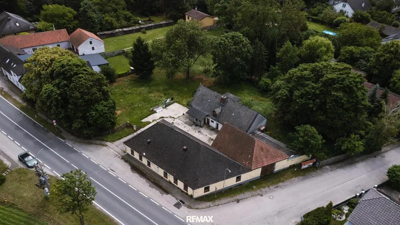 Luftaufnahme eines Anwesens mit mehreren Gebäuden und viel Grünfläche an einer Straße.