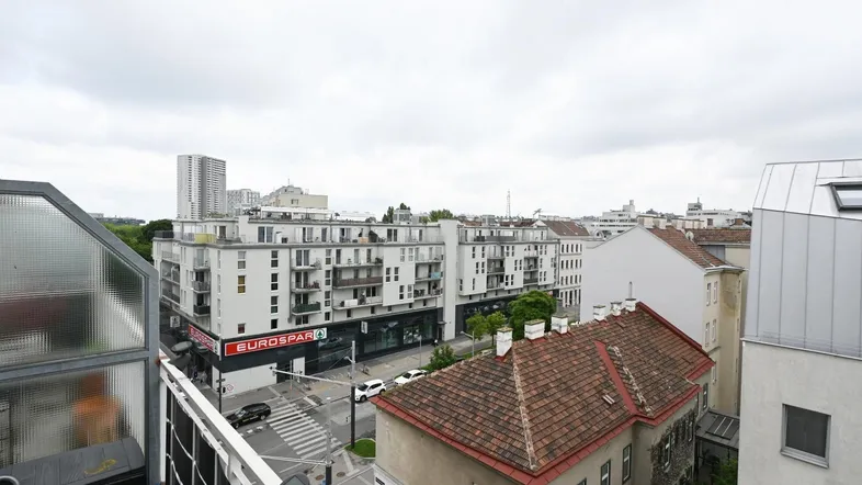Blick über die Dächer der Stadt mit modernen Gebäuden und einem Supermarkt im Vordergrund.
