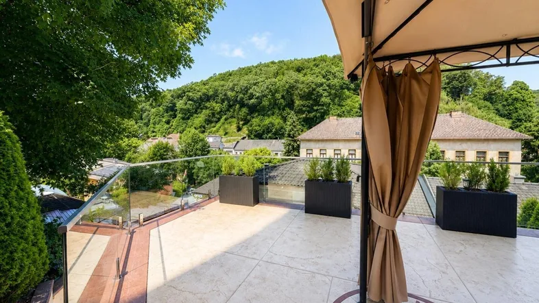 Große Terrasse mit Glasgeländer, Pergola und weitem Blick auf die bewaldeten Hügel.