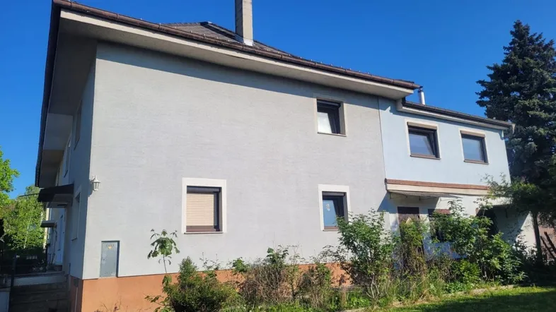Außenansicht eines Einfamilienhauses mit hellgrauer Fassade, braunem Sockel und Satteldach.