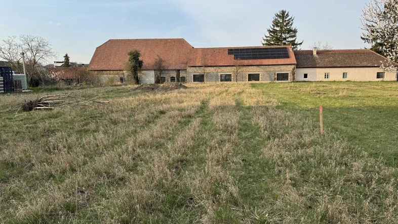 Altes Bauernhaus mit rotem Ziegeldach und Solarpaneelen, umgeben von einer weiten Wiese.