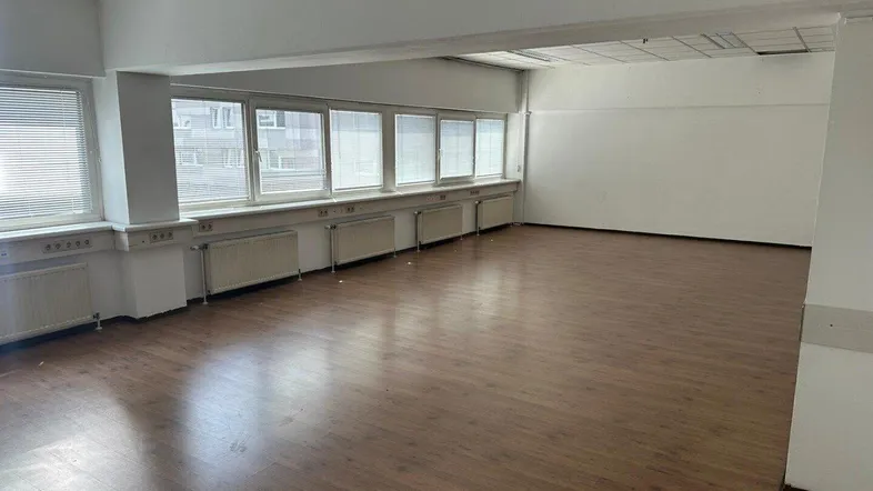 Geräumiger, leerer Büroraum mit vielen Fenstern, Heizkörpern und Laminatboden, bereit zur individuellen Gestaltung.