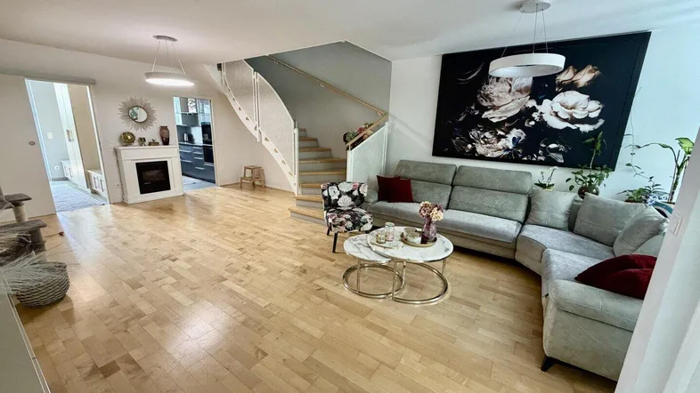 Geräumiges Wohnzimmer mit hellem Parkettboden, bequemer Sitzecke und modernem Kamin.