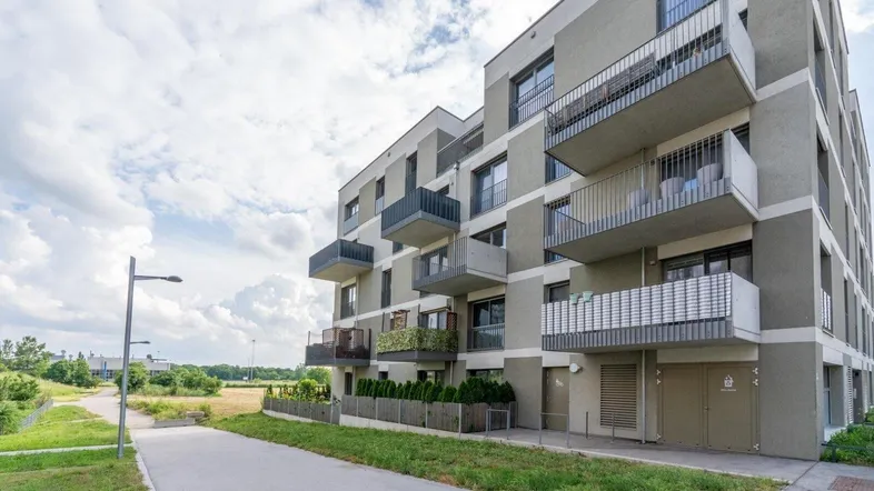 Modernes Mehrfamilienhaus mit Balkonen und gepflegter Außenanlage unter bewölktem Himmel.