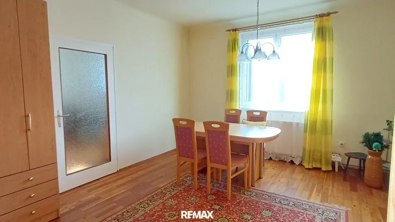 Heller Essbereich mit Holztisch, Stühlen, Holzschrank und Fenster mit gelben Vorhängen.